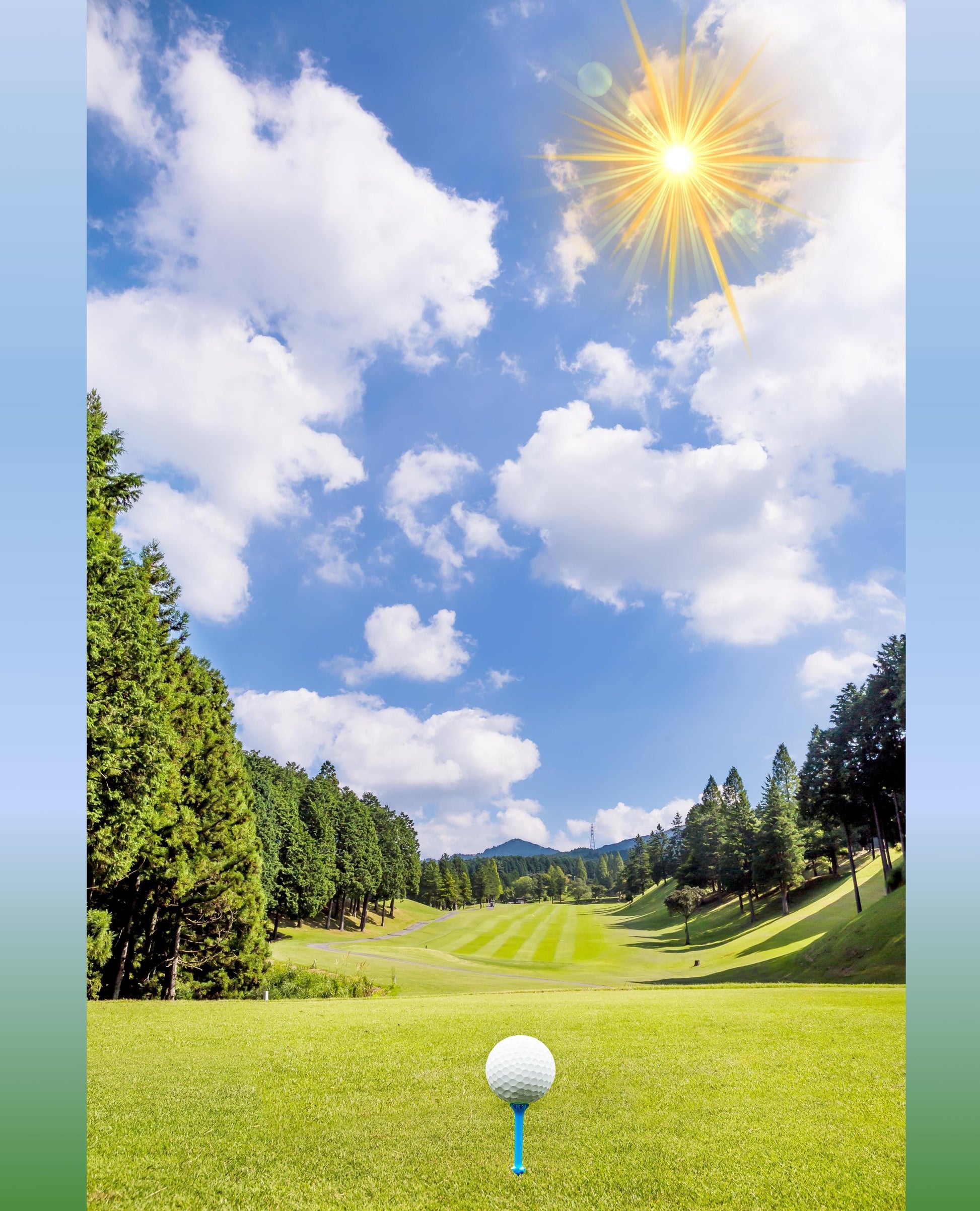 May include: A white golf ball on a blue tee on a green golf course. The golf course is surrounded by trees and the sky is blue with white clouds and a bright sun.